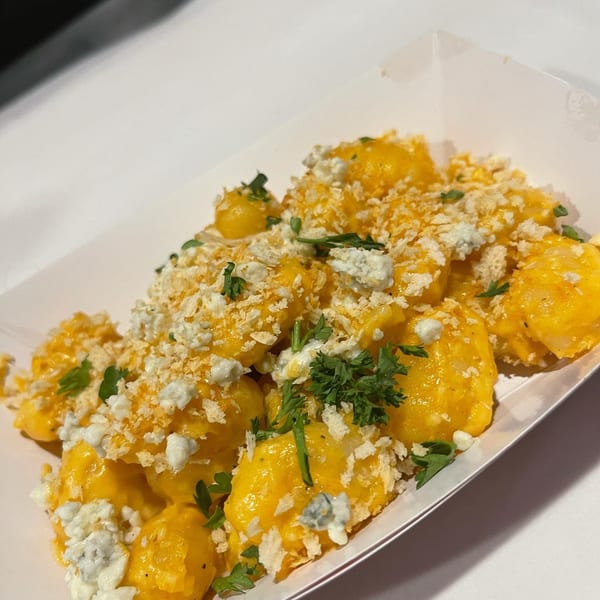 Gnocchi mac and cheese with blue cheese crumbles, breadcrumbs, and parsley in a white container.